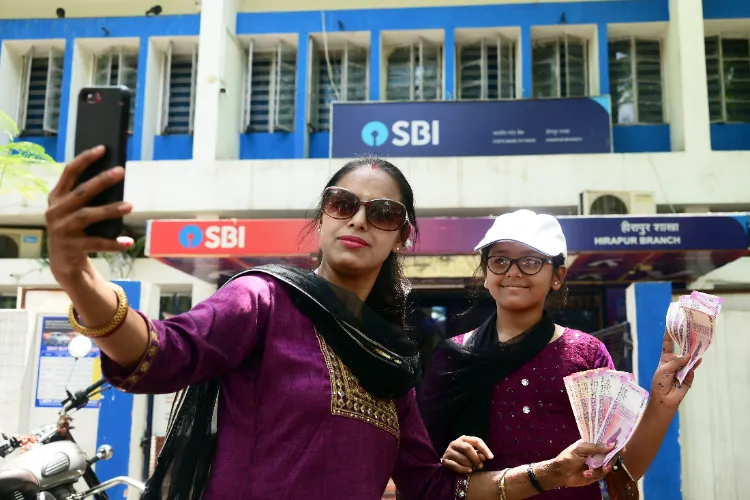 Women posing for a selfie with a Rs 2000 denomination currency note