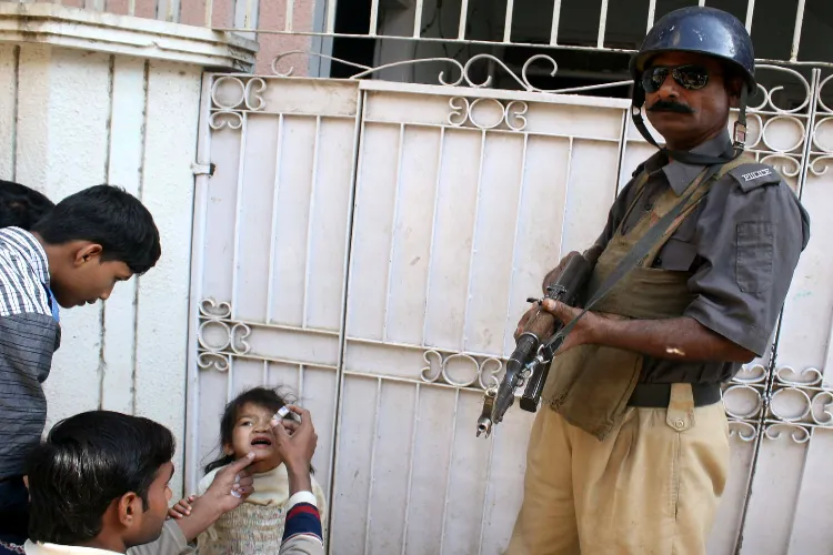 A Pakistan policeman stands guard as a health worker vaccinates a girl against polio during a door-to-door vaccination campaign in southern Pakistan's Karachi